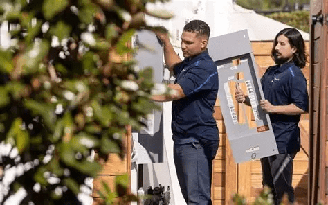Two technicians installing an electrical panel outdoors